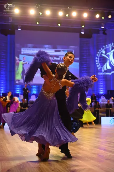 Dancesport competitor: Female dancer: purple ballgown with a sequined/beaded bodice and large purple fe