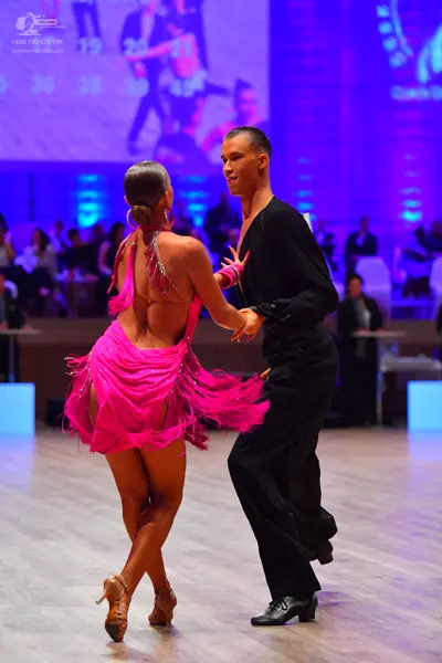 Dancesport competitor: Female dancer: bright pink latin dress with sequins and long fringe, wearing lar