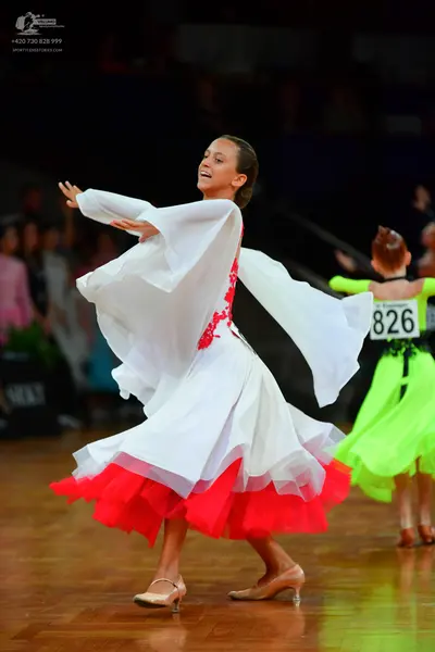Dancesport competitor: Female dancer 1: white flowing dress with large, wide sleeves and a red layer at