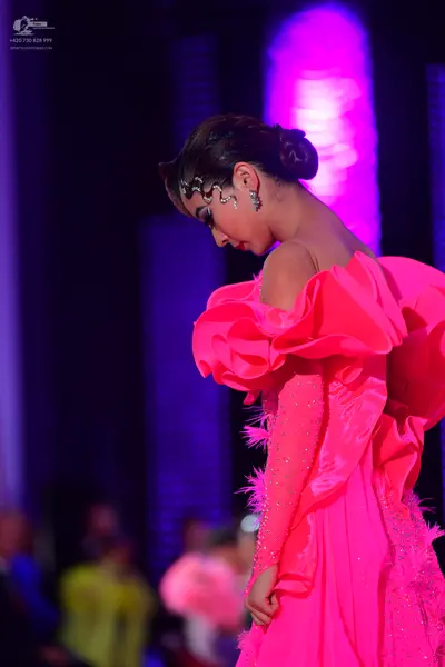Dancesport competitor: Female dancer: bright pink ballroom dress featuring large, dramatic ruffles, shi