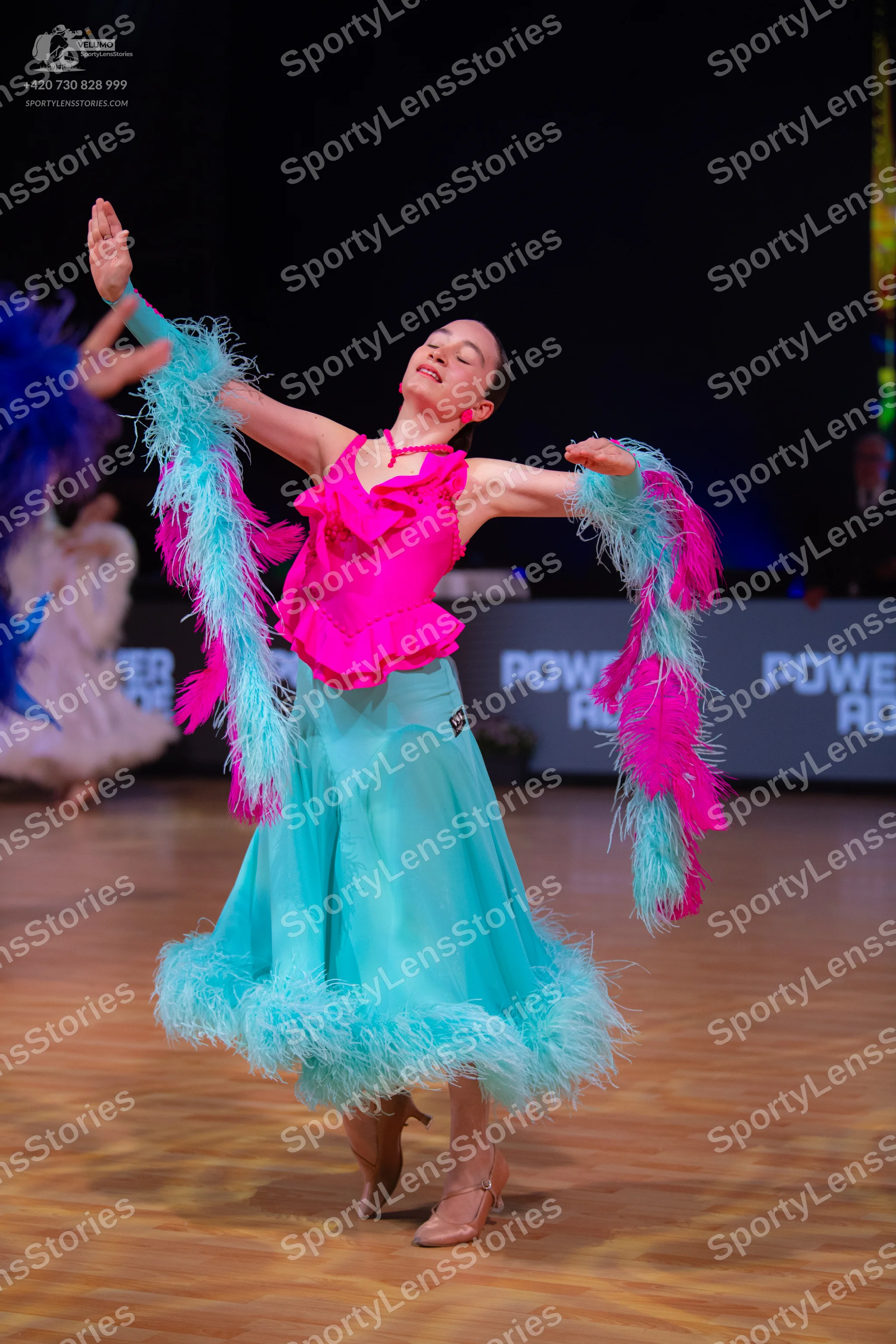Dancesport competitor: Female dancer: bright pink ruffled top with a long, flowing light blue skirt fea