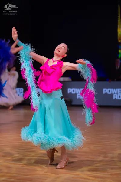 Dancesport competitor: Female dancer: bright pink ruffled top with a long, flowing light blue skirt fea