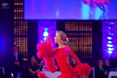 Dancesport competitor: Female dancer: red Latin dance dress with large red feather accents on the sleev