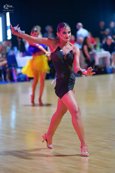 Dancesport competitor: Female dancer in foreground: black latin dance dress with silver sparkly wristba