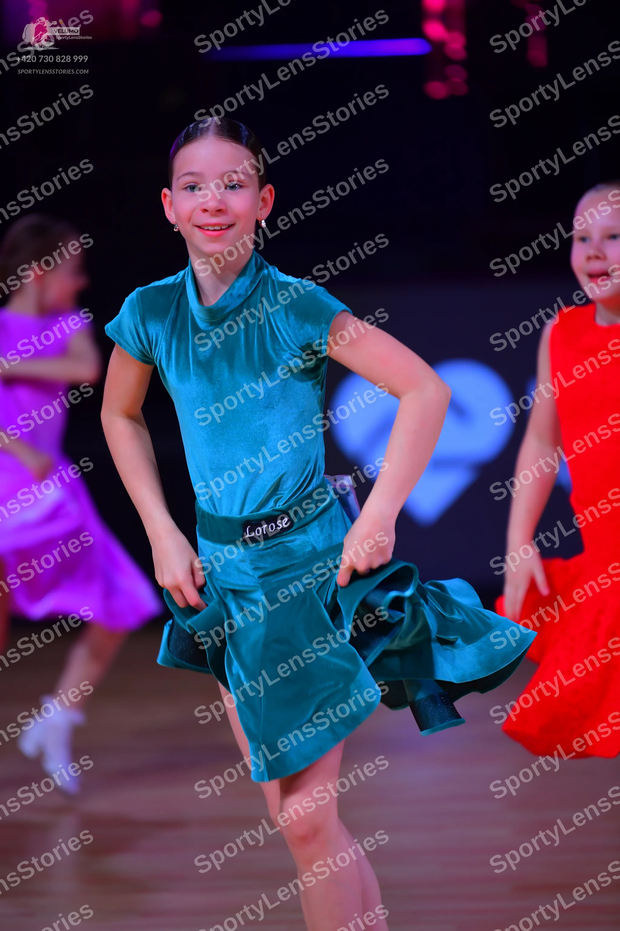 Dancesport competitor: Female dancer in center: teal satin short dress with a high neck and short sleev
