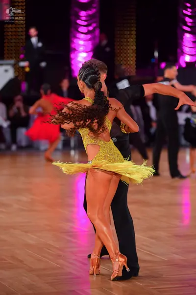 Dancesport competitor: Female dancer in foreground: yellow sequin latin dress with fringe and tan dance