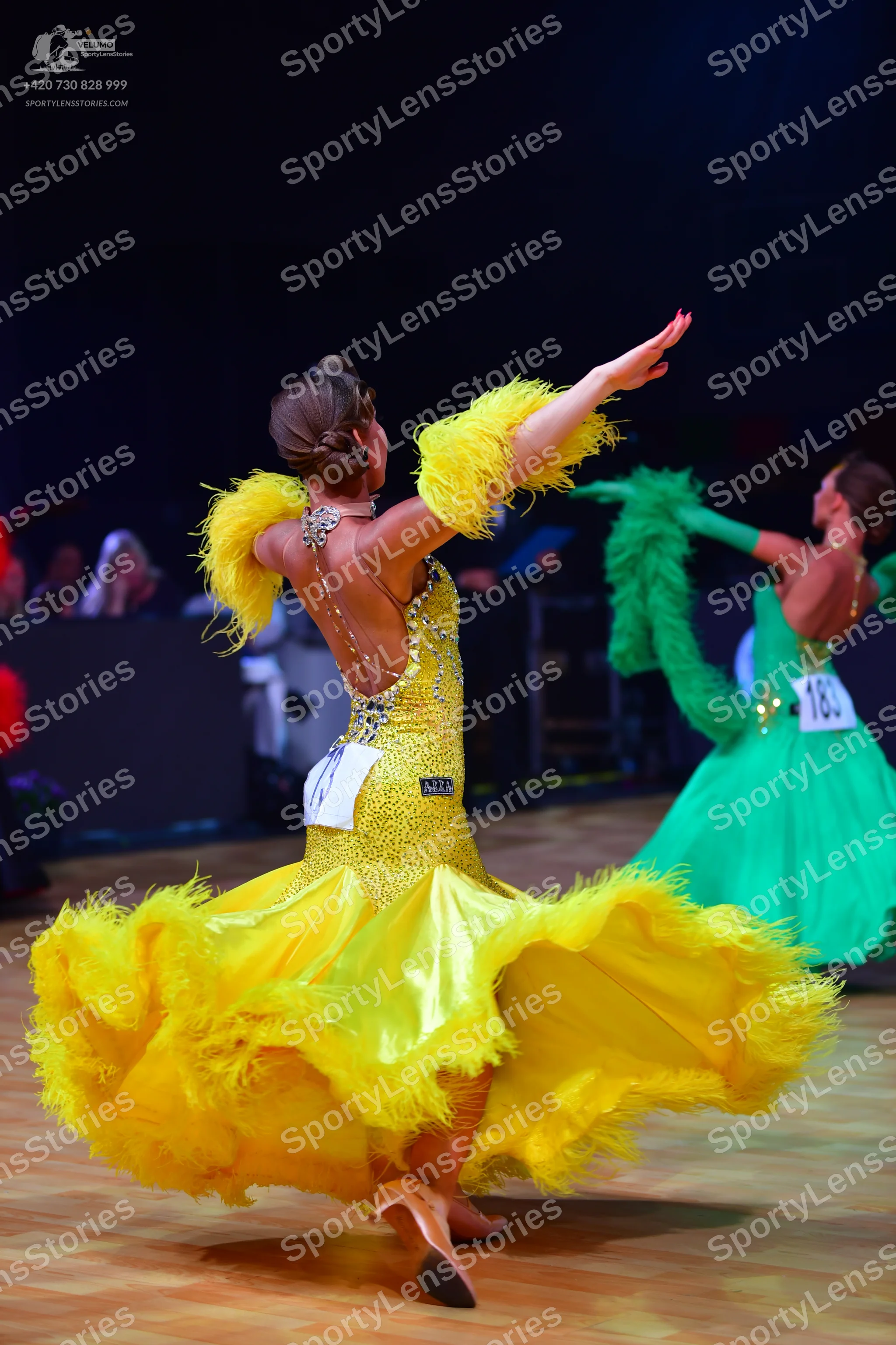 Dancesport competitor: Female dancer in foreground: yellow ballroom gown with a sequined bodice and lar