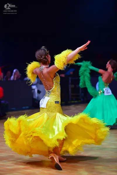 Dancesport competitor: Female dancer in foreground: yellow ballroom gown with a sequined bodice and lar