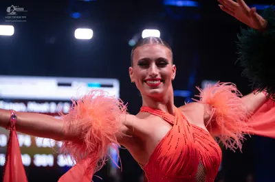 Dancesport competitor: Female dancer: orange latin dress with sequins and feather details on the sleeve