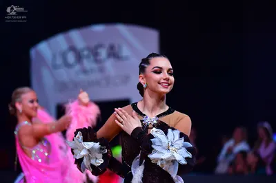Dancesport competitor: Female dancer in foreground: black latin dance dress featuring large white fabri