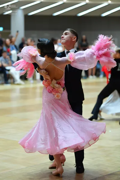Dancesport competitor: Female dancer: pink ballgown with large pink floral embellishments, pink feather