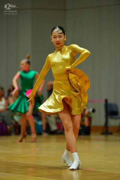Dancesport competitor: Female dancer in foreground: gold metallic long-sleeved latin dress with a flare