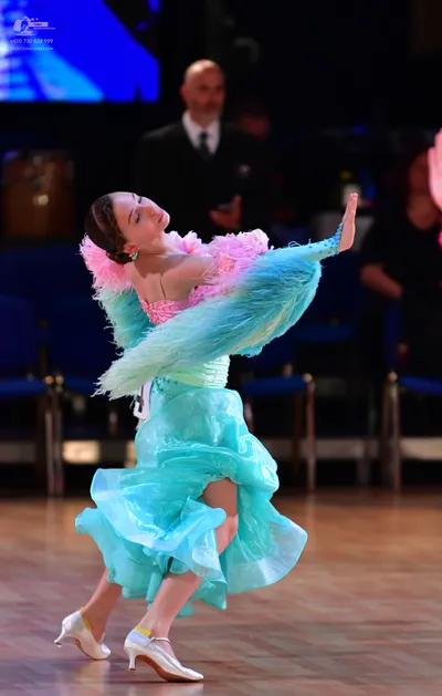 Dancesport competitor: Female dancer: light blue ballgown with many layers of ruffled fabric, pink feat