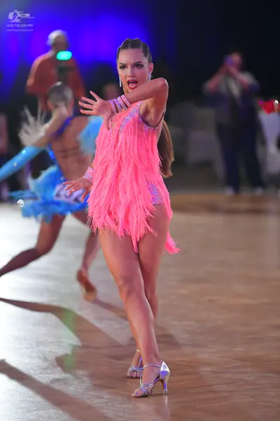 Dancesport competitor: Female dancer in foreground: bright pink Latin dance dress with fringe