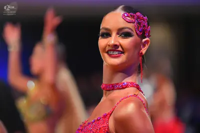Dancesport competitor: Female dancer in foreground: pink/magenta latin costume with heavy sequin/bead e