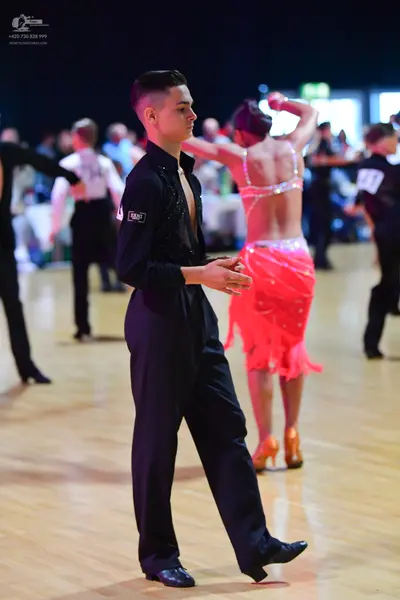Dancesport competitor: Male dancer in foreground: black long-sleeve shirt and black trousers