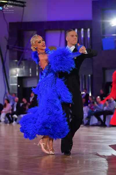 Dancesport competitor: Female dancer: bright blue voluminous dress with heavy feather or fringe texture