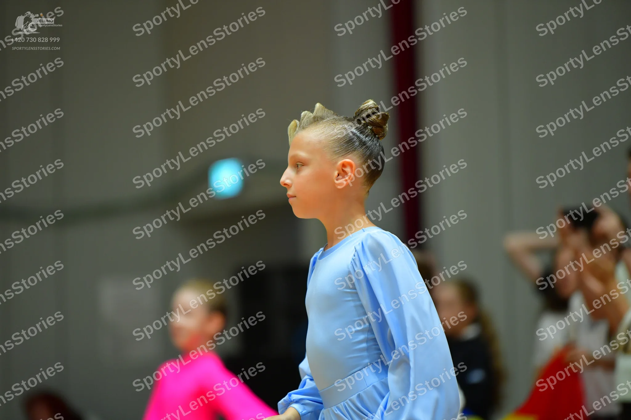 Dancesport competitor: Female dancer in foreground: light blue long-sleeved dress with smooth, shiny fa