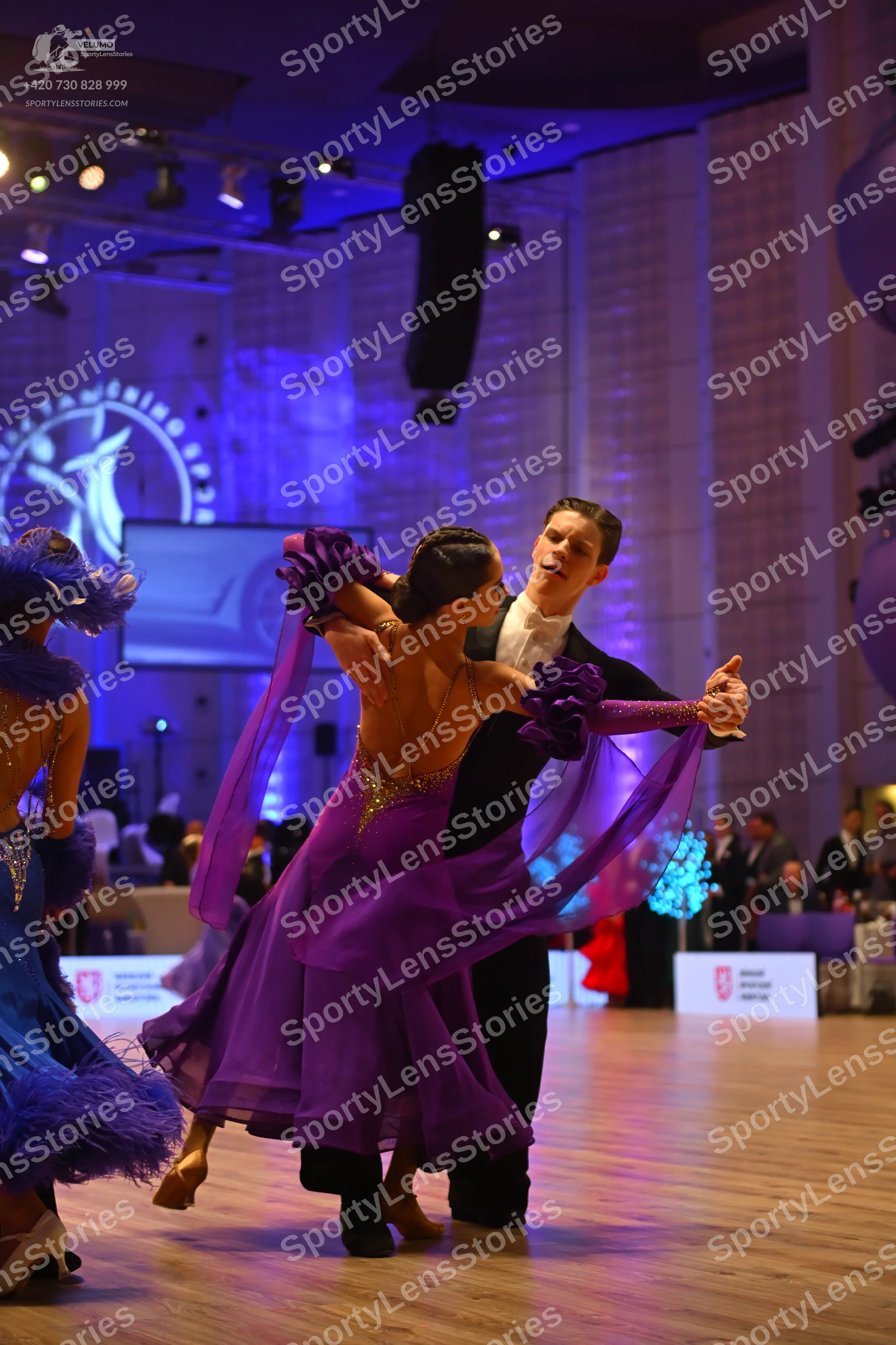 Dancesport competitor: Female dancer in center: purple latin dress with a sparkly bodice, flowing skirt