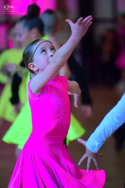 Dancesport competitor: Female dancer in foreground: bright pink sleeveless dress with a full, flowing s