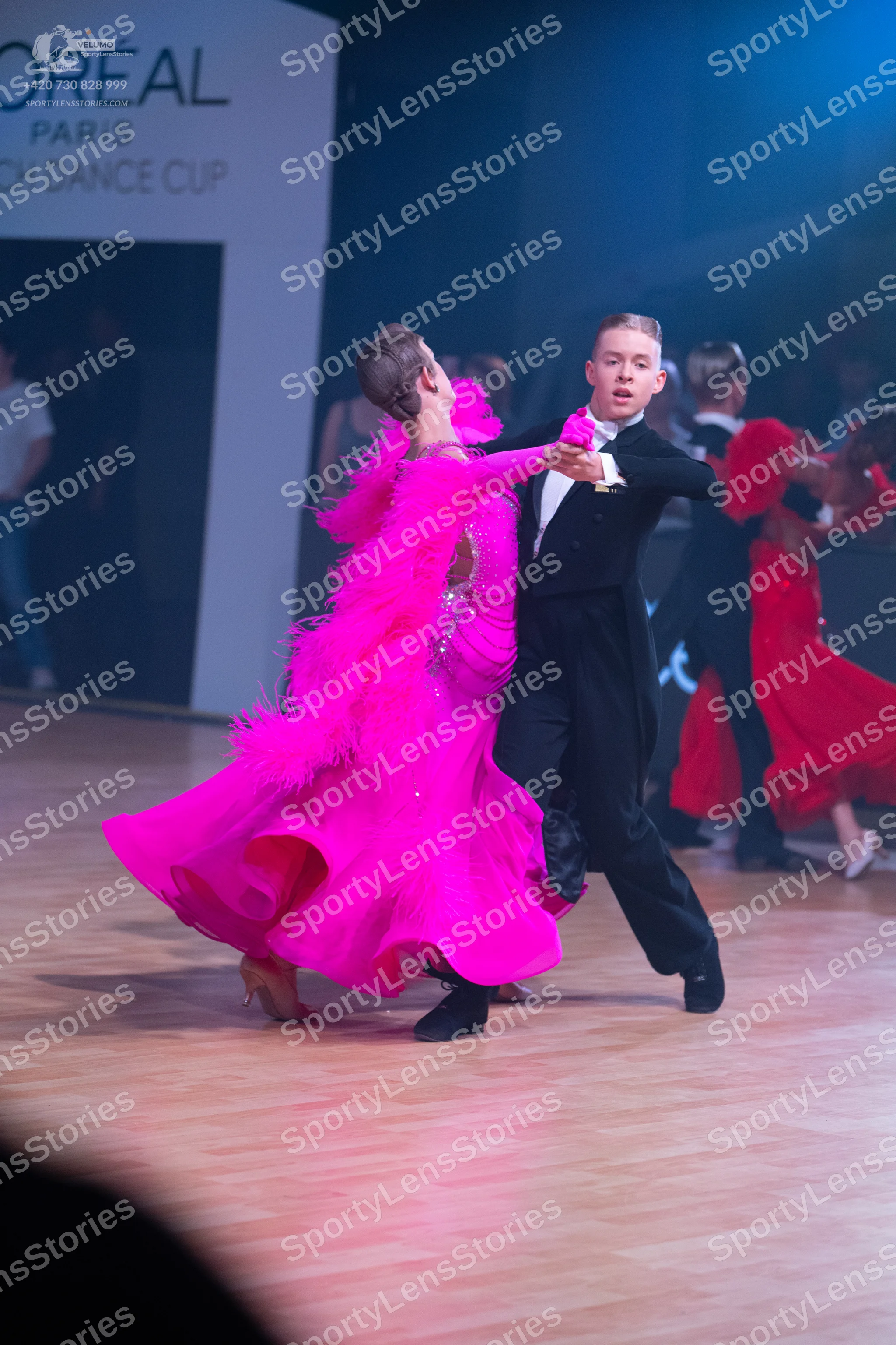 Dancesport competitor: Female dancer in foreground: bright pink ballroom gown with voluminous ruffled o