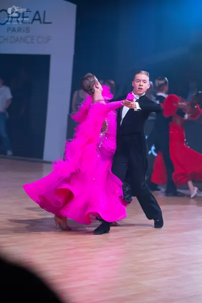Dancesport competitor: Female dancer in foreground: bright pink ballroom gown with voluminous ruffled o