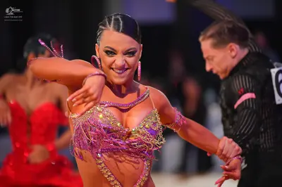 Dancesport competitor: Female dancer in foreground: pink, gold, and lavender sequined Latin dress with 