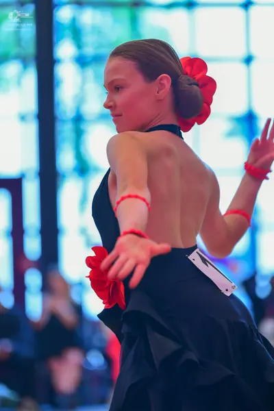 Dancesport competitor: Female dancer: black latin dress with red flower hair accessory and red wristban