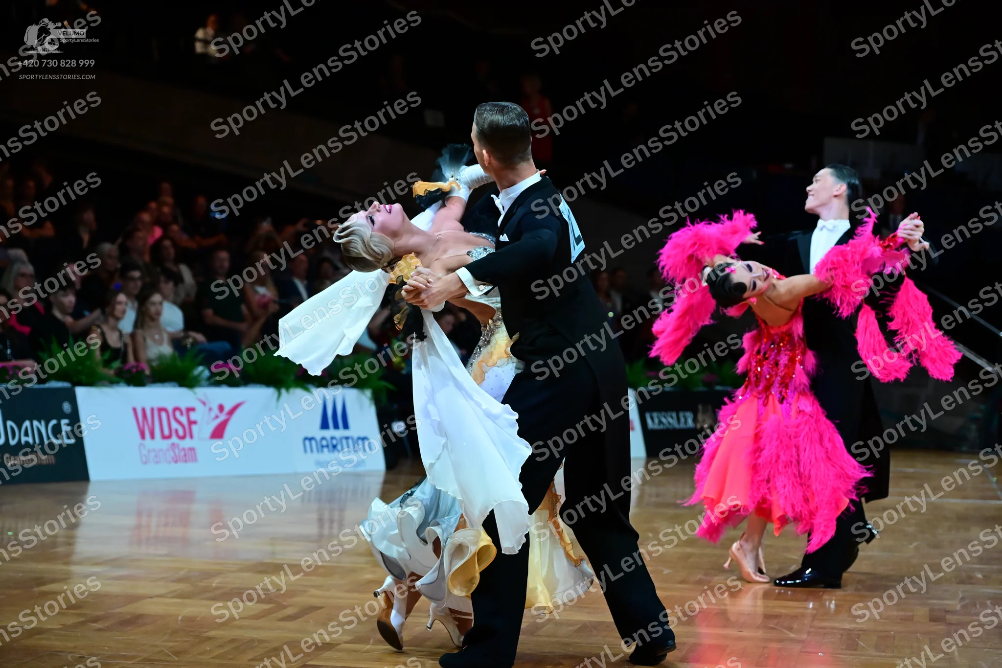 Dancesport competitor: Foreground female dancer: white and gold flowing ballroom gown