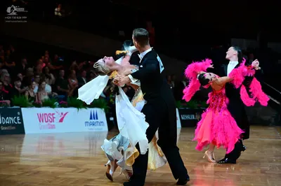 Dancesport competitor: Foreground female dancer: white and gold flowing ballroom gown