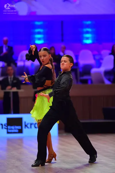 Dancesport competitor: Female dancer: black top with long bell sleeves and a neon yellow/green fringe s