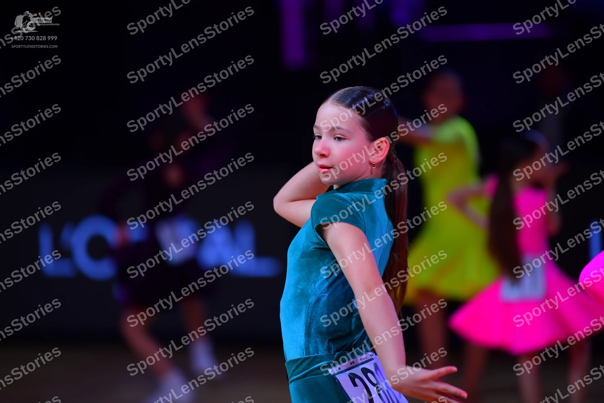 Dancesport competitor: Female dancer in foreground: teal satin Latin dress with short sleeves