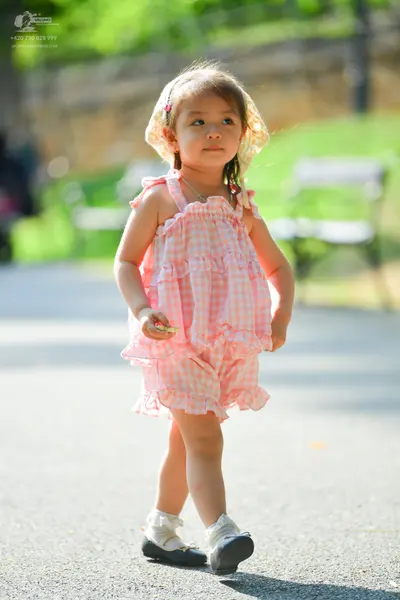 Dancesport competitor: The child is wearing a pink and white gingham patterned sleeveless ruffled top a