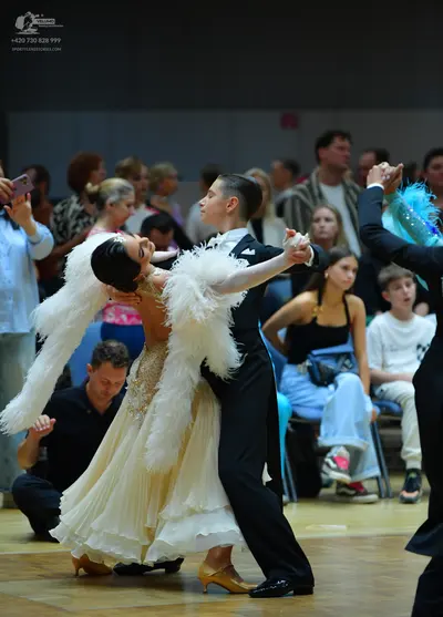 Dancesport competitor: Female dancer: cream-colored ballroom gown with a sequined bodice and large whit