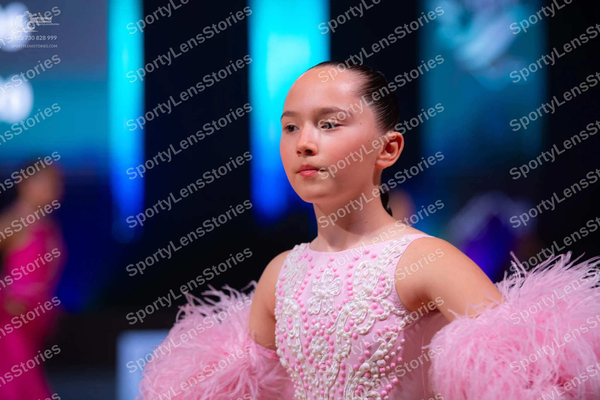 Dancesport competitor: Female dancer in foreground: light pink sleeveless costume decorated with white