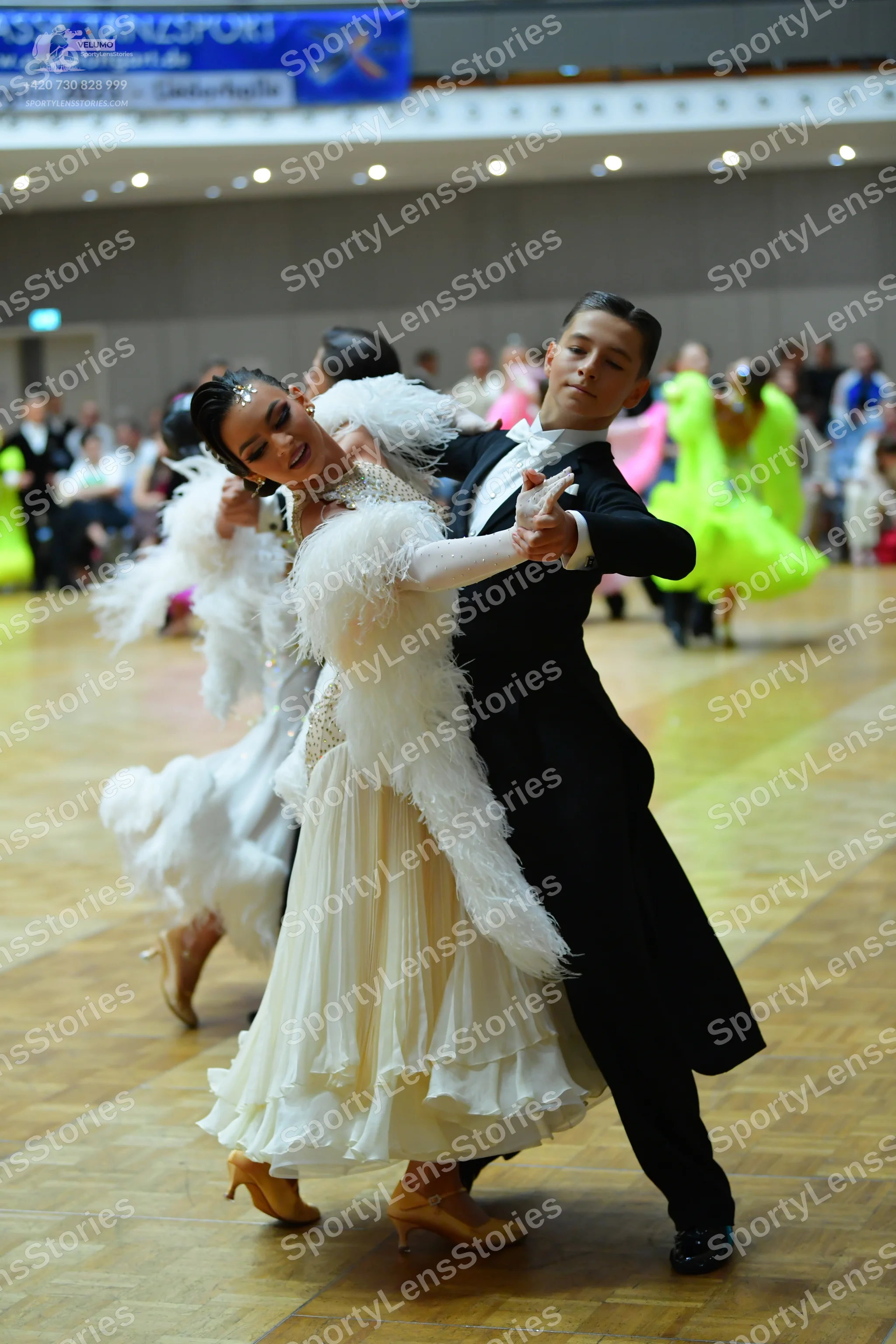 Dancesport competitor: Female dancer: white ballgown with large white feather trim on the bodice and a