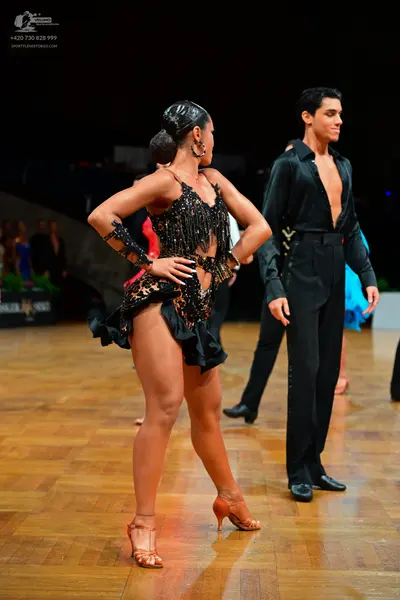 Dancesport competitor: Female dancer: black Latin dress with gold sequins, fringe, and a matching arm c