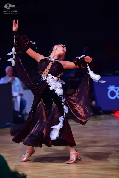 Dancesport competitor: Female dancer: dark brown Latin dance dress with long flowing sleeves, lattice-s