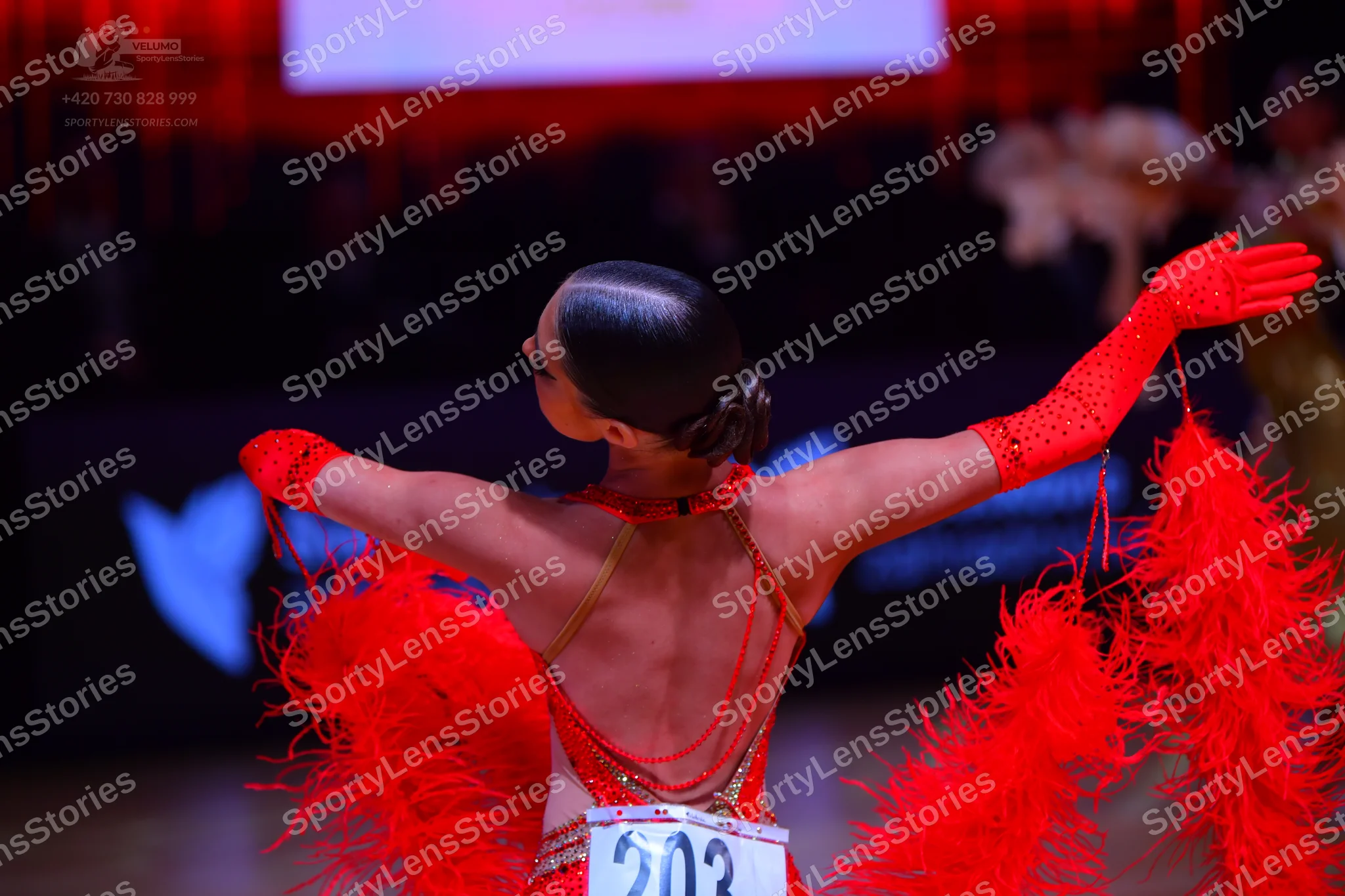 Dancesport competitor: Female dancer: red Latin dress with large red feather accents, sequins, and thin