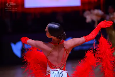 Dancesport competitor: Female dancer: red Latin dress with large red feather accents, sequins, and thin