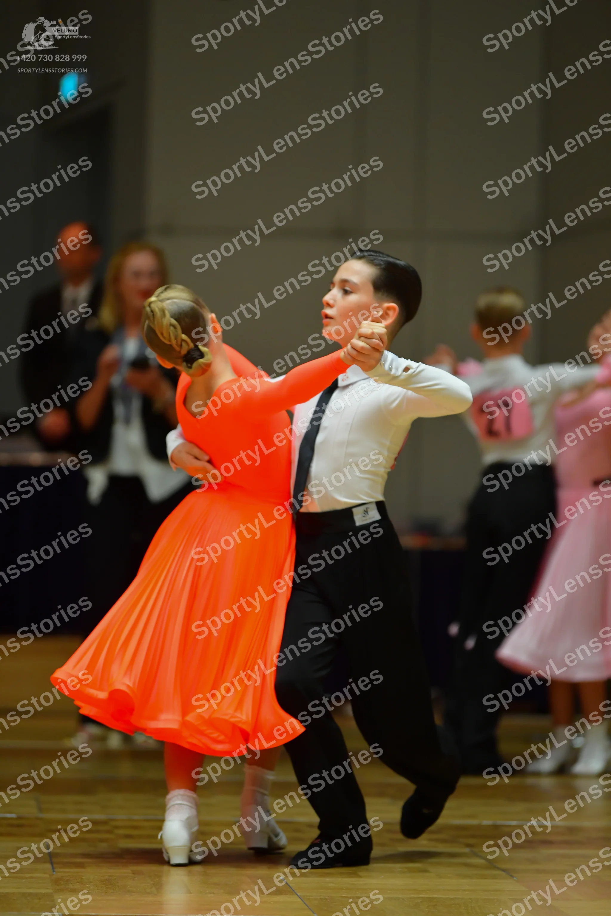 Dancesport competitor #27: Female dancer in foreground: bright orange long-sleeved ballroom dress with a fu