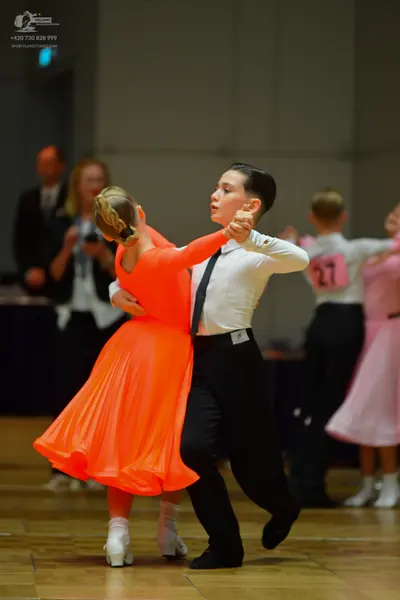 Dancesport competitor #27: Female dancer in foreground: bright orange long-sleeved ballroom dress with a fu