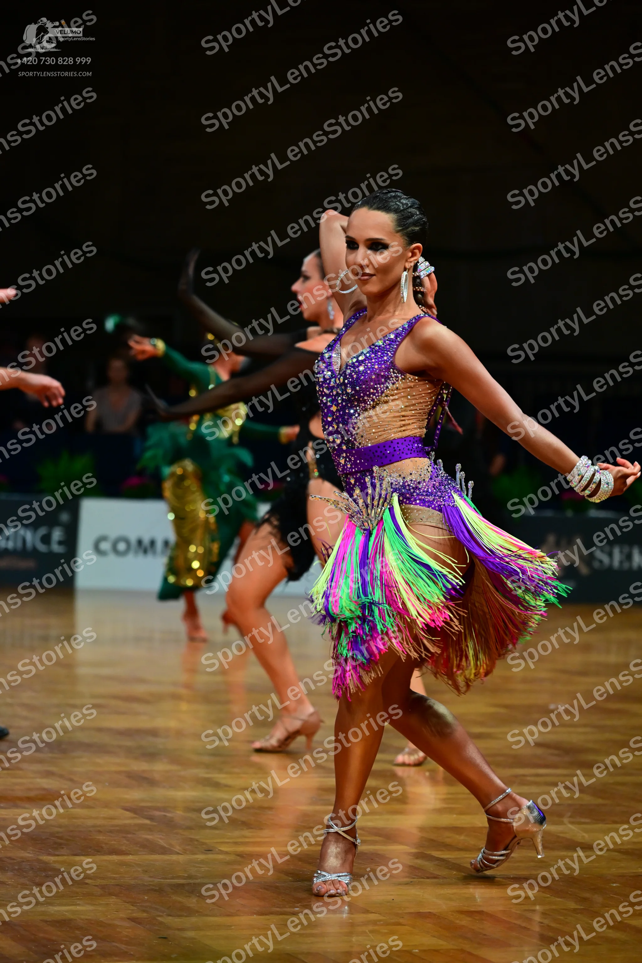 Dancesport competitor: Female dancer (foreground): purple and nude latin dress with multi-colored fring