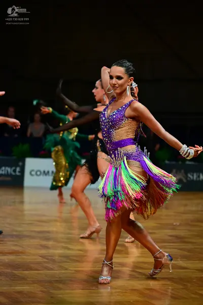 Dancesport competitor: Female dancer (foreground): purple and nude latin dress with multi-colored fring