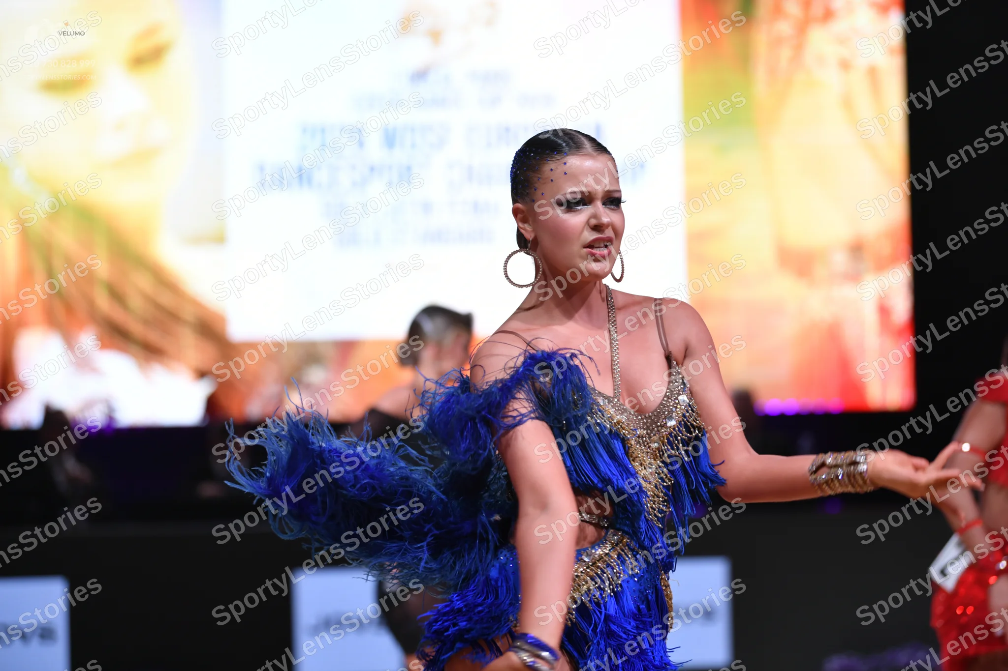 Dancesport competitor: Female dancer (center): Blue and gold Latin dance dress featuring heavy blue fri