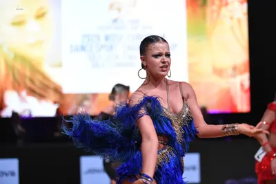 Dancesport competitor: Female dancer (center): Blue and gold Latin dance dress featuring heavy blue fri