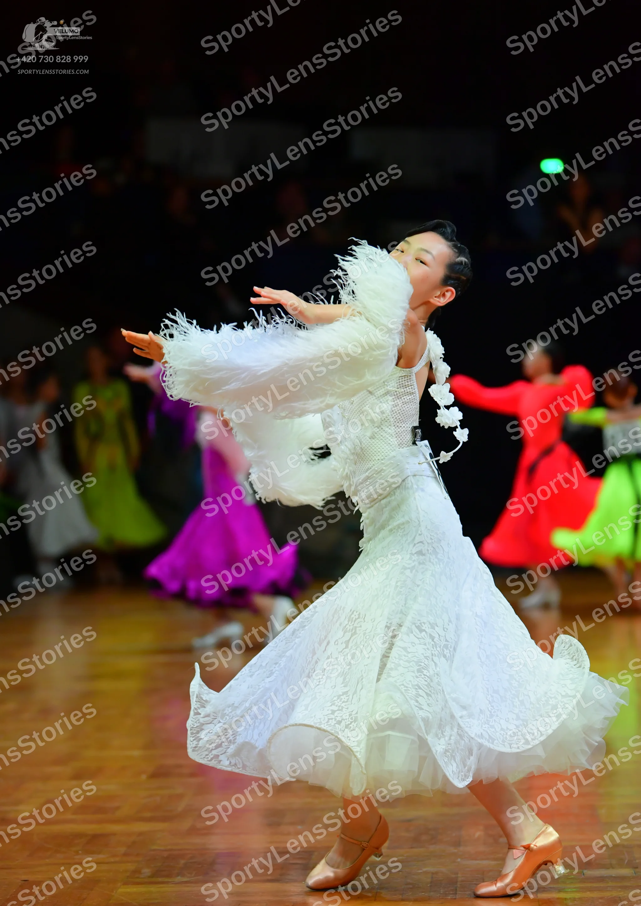 Dancesport competitor: Female dancer in foreground: white lace ballroom gown with large, voluminous whi