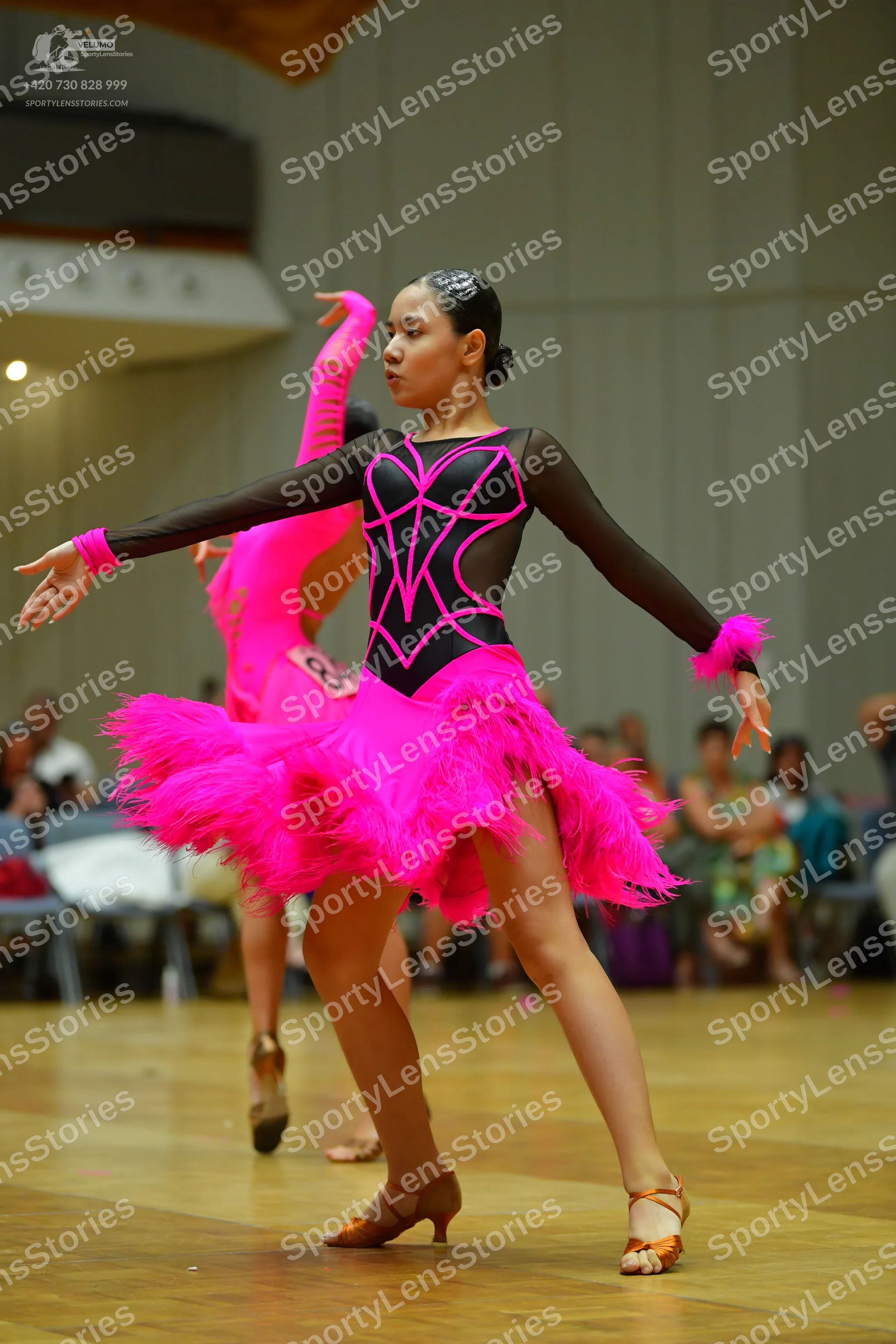 Dancesport competitor: Female dancer in foreground: black long-sleeved Latin dress with pink geometric
