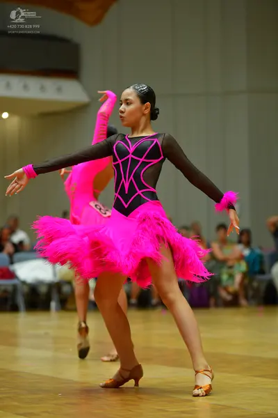 Dancesport competitor: Female dancer in foreground: black long-sleeved Latin dress with pink geometric 