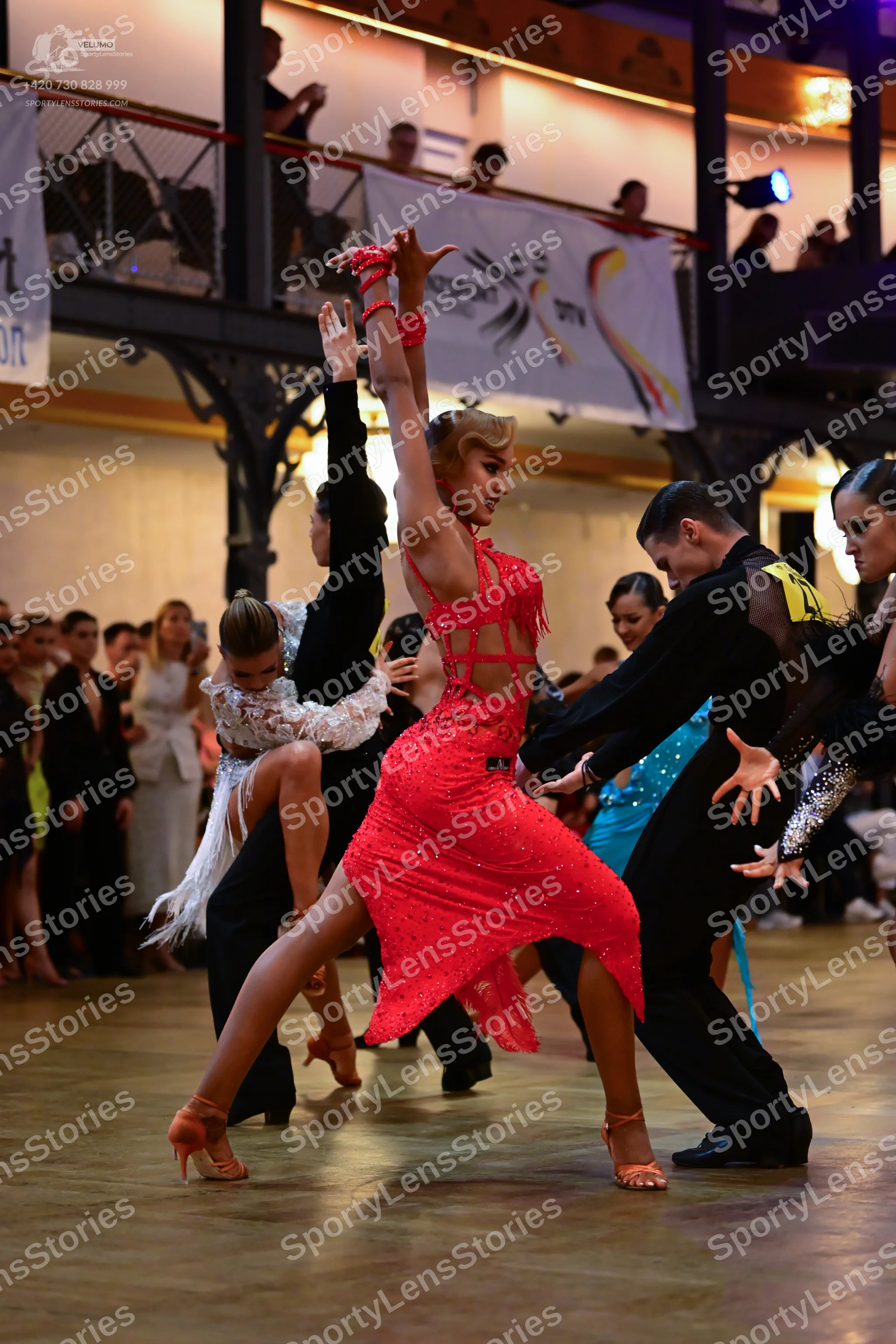 Dancesport competitor: Female dancer in center: red Latin dress with sequins and sheer mesh details